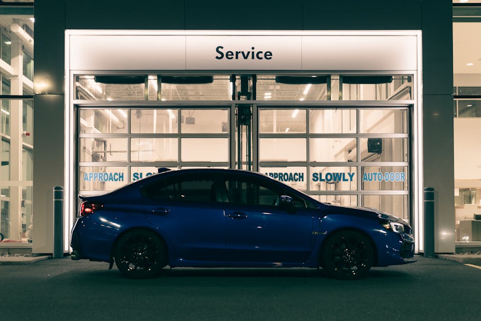 A sleek blue car parked outside an illuminated garage service door at night.