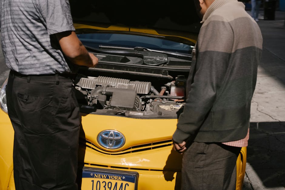 Two men examining the engine of a yellow taxi on a sunny day in New York City.