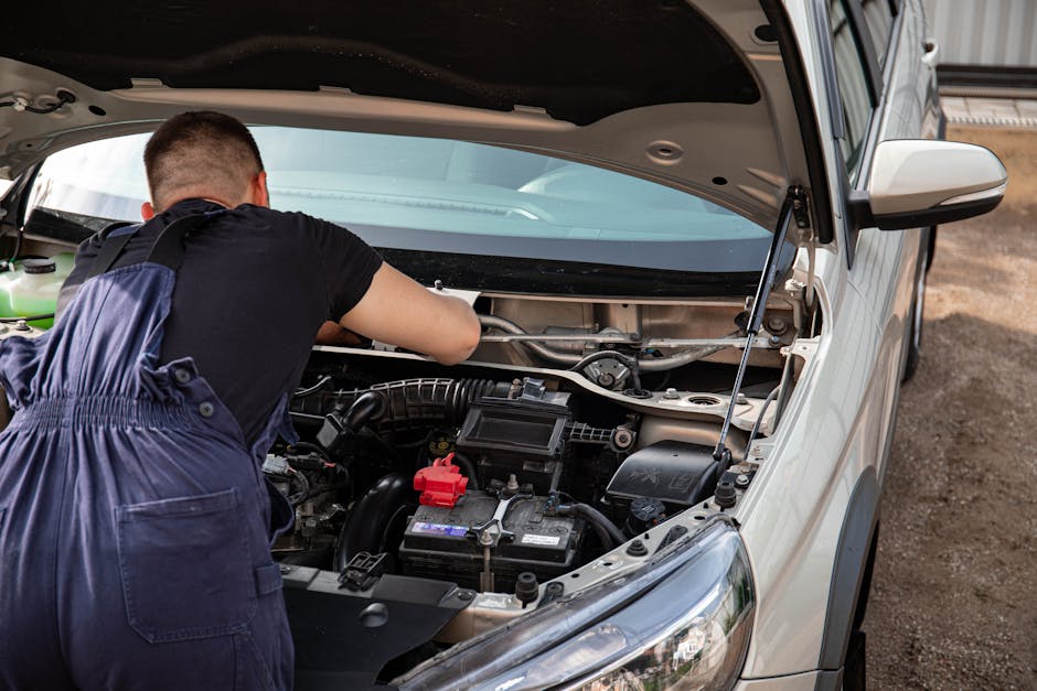 A mechanic fixes a car engine outdoors, focusing on vehicle maintenance.